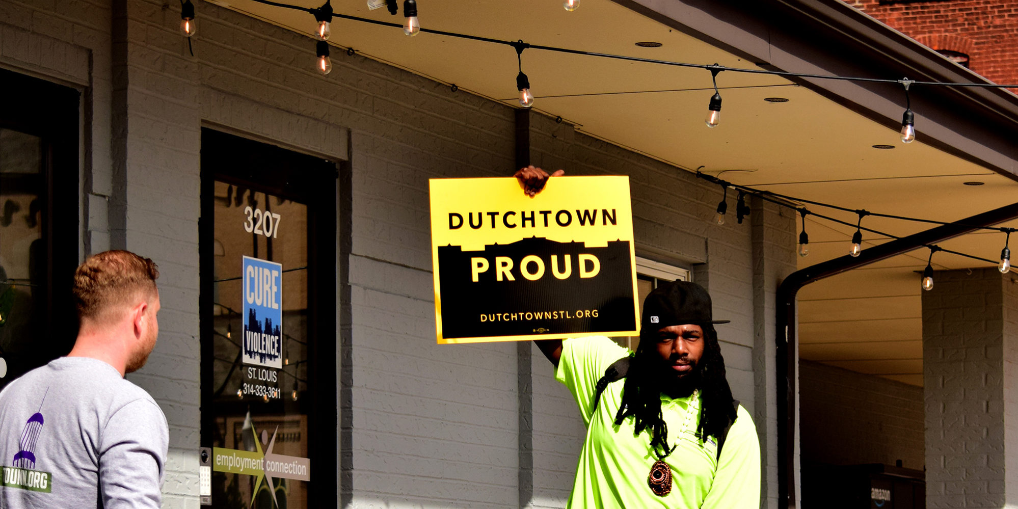 A Dutchtown neighbor holds a Dutchtown Proud sign in front of the Neighborhood Innovation Center in Downtown Dutchtown, St. Louis, MO.