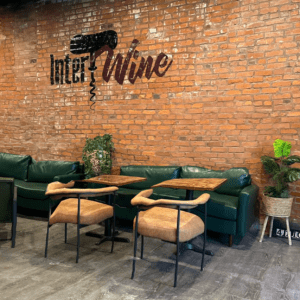 The interior of IntertWine Wine Bar at 4710 Virginia Avenue in Dutchtown, St. Louis, MO. The interior features a large exposed brick wall emblazoned with the IntertWine logo, green leather sofas, and modern lounge chairs.