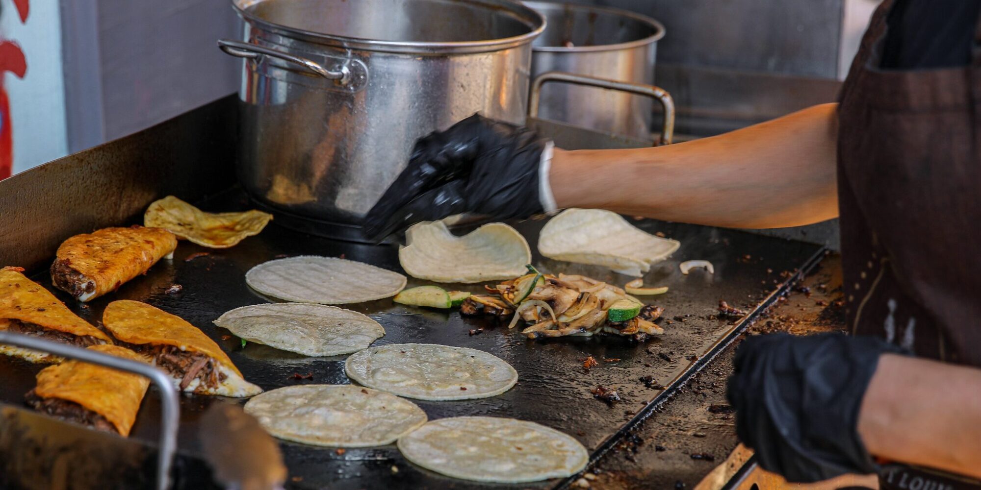 Tacos La Jefa's birria tacos and tortillas being prepared on a flat top grill at Urban Eats Food Day in Dutchtown, St. Louis, MO.