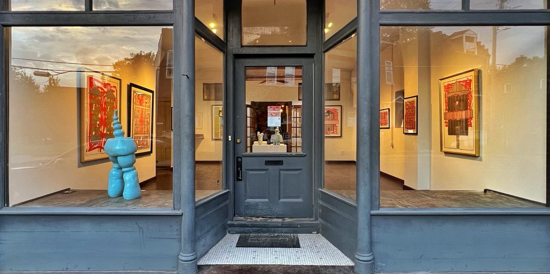 The storefront of Wildfruit Projects, a queer-led art space at 4704 Virginia Avenue in Dutchtown, St. Louis, MO. An abstract blue sculpture is visible in the left window, and large red, gold,, and black paintings can be seen on the gallery walls.